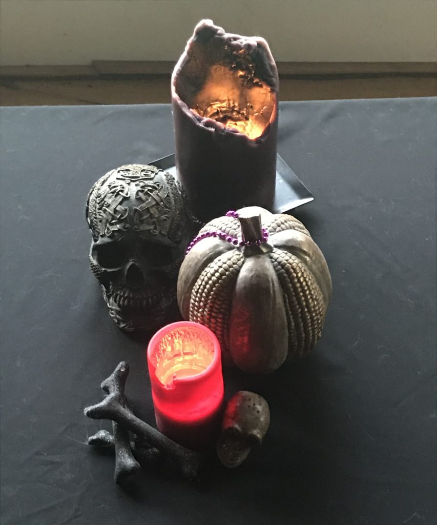 An altar with a black cloth, two candles, a resin skull, and some glittery faux bones